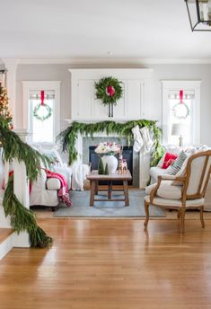 a living room decorated for christmas with white furniture and greenery on the mantel