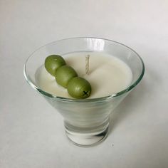 two green olives are sitting in a glass bowl next to a white candle on a table