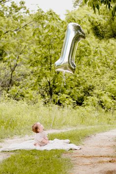 a baby laying on the ground with a silver balloon