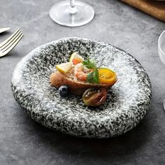 a black and white plate topped with food next to two glasses of wine on top of a table