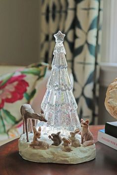 a glass christmas tree sitting on top of a wooden table next to a book shelf