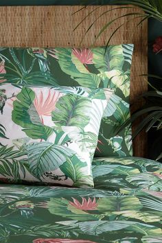 a bed covered in green and pink tropical print sheets with plants on the headboard