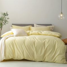 a bed with yellow sheets and pillows in a room next to a potted plant