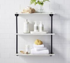 two shelves with towels, soaps and other items on them in a white tiled bathroom