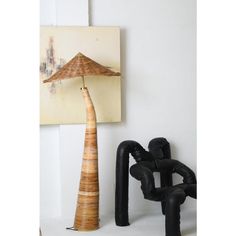 a wooden lamp sitting next to a black chair and painting on the wall behind it