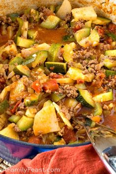 a pot filled with meat and vegetables on top of a red cloth next to a spoon