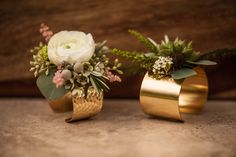 two gold vases with flowers and greenery in them