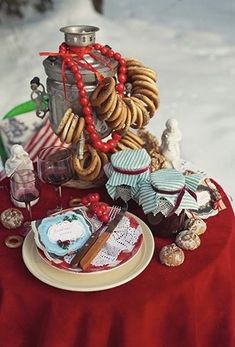 a red table topped with lots of desserts and cookies on top of a snow covered ground