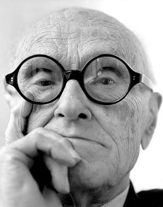 an old man wearing glasses and holding his hand to his face while looking at the camera