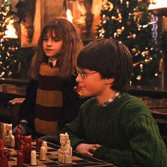 two children playing chess in front of christmas trees