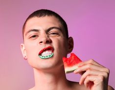 a young man is eating a piece of watermelon with his teeth painted green