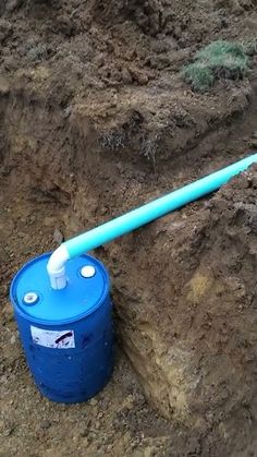 a blue barrel sitting in the middle of some dirt with a pipe sticking out of it