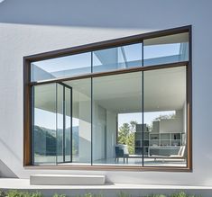 an open window on the side of a white building with grass and bushes in front of it