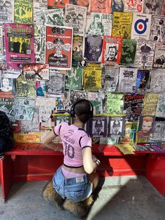 a woman sitting at a red bench in front of a wall covered with posters