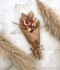 a bouquet of dried flowers wrapped in brown paper and feathers on a white surface with water droplets