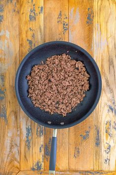 a frying pan filled with ground beef on top of a wooden table