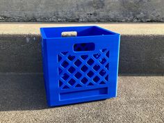 a blue trash can sitting on the side of a sidewalk next to a cement wall