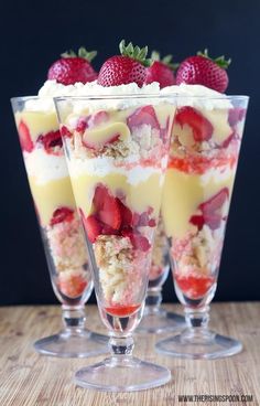 three desserts with strawberries and cream in glasses on a wooden table, ready to be eaten