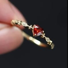 a person holding a ring with a red stone in it's center and two white diamonds on the side