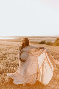 a pregnant woman in a white dress is walking through a field with her long flowing fabric