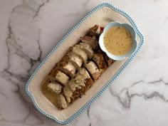 a white plate topped with meat covered in gravy next to a bowl of sauce