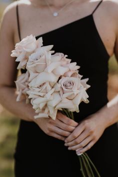 a woman in a black dress holding a bouquet of white and pink flowers on her left arm