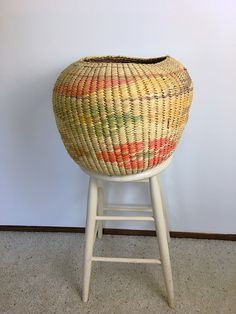 a woven basket sitting on top of a wooden stool next to a wall and floor