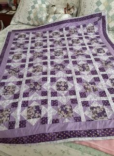 a purple quilt is laying on top of a bed