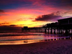 a pier at sunset with the sun setting over the water and clouds in the sky