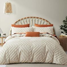 a white bed with orange pillows in a bedroom next to a potted plant on the floor