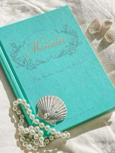 a blue book with pearls and sea shells on the cover next to two seashells