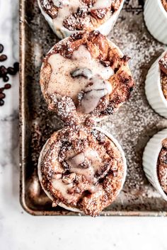 cinnamon rolls with icing and powdered sugar are on a baking tray next to coffee beans