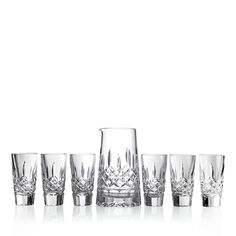 an assortment of crystalware on a white background with reflection in the glass, including one vase and six glasses