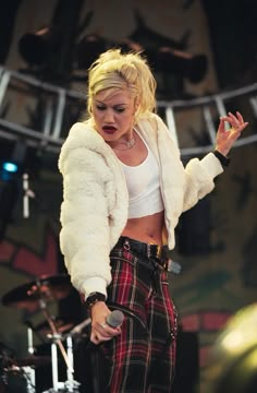 a woman standing on top of a stage with her hands in the air and wearing plaid pants