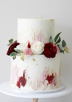 a white cake with red and pink flowers on it sitting on top of a table