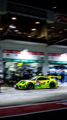 a yellow sports car driving down the street in front of a gas station at night