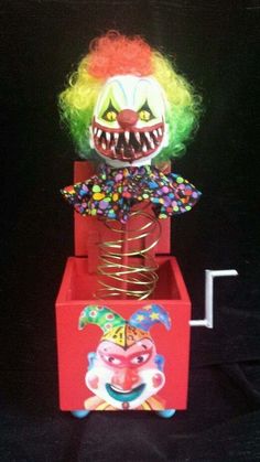 a clown head sitting on top of a red box with spirals in it's mouth