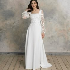 a woman in a white wedding dress standing on a wooden floor with her arms behind her head