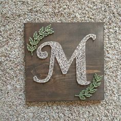 a wooden sign with the letter m made out of wire and leaves on top of it