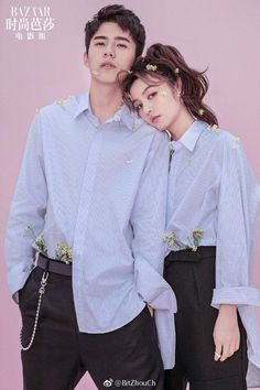 two people standing next to each other in front of a pink wall wearing blue shirts and black pants