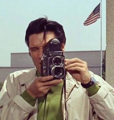 a man taking a selfie with his camera in front of an american flag and building