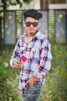 a young boy wearing sunglasses and standing in the middle of some grass with his hands on his hips