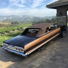 a brown and black car parked in front of a house on top of a hill