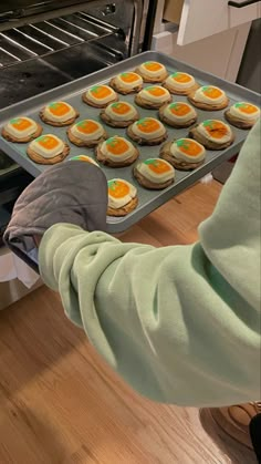 a person holding a tray of cookies in front of an oven