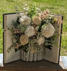 an open book with flowers on it sitting on a table in front of some grass