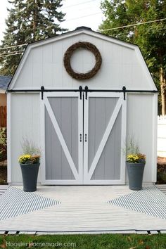 a white shed with two doors and a wreath on the door