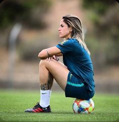 a female soccer player sitting on the ground with her legs crossed and looking off to the side