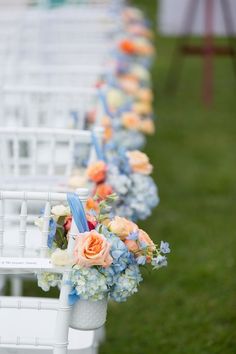 rows of white chairs with blue and orange flowers lining the back of each chair for an outdoor ceremony