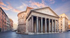 an old building with columns and pillars in the middle of a city street at sunset