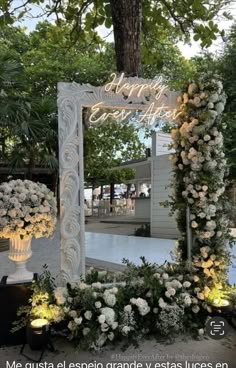 a white mirror sitting on top of a table covered in flowers and greenery next to a tree